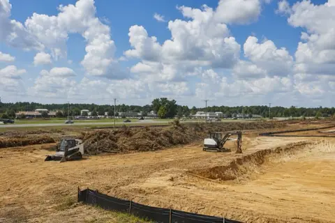 Mulcher and dozer opening a large commercial tract beside a four-lane road, windrows and silt fence in place